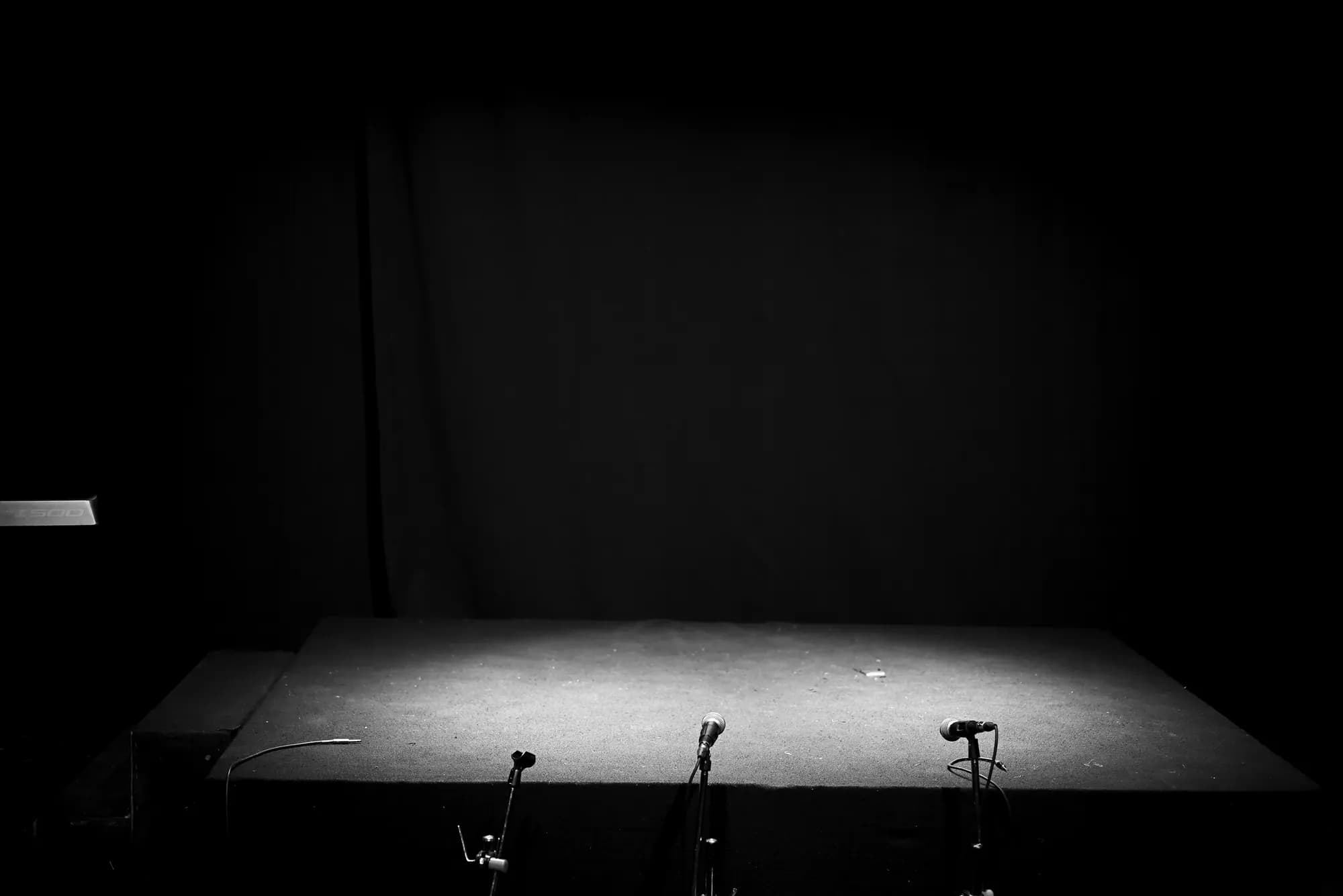 An empty stage lit by a single spotlight, microphones waiting